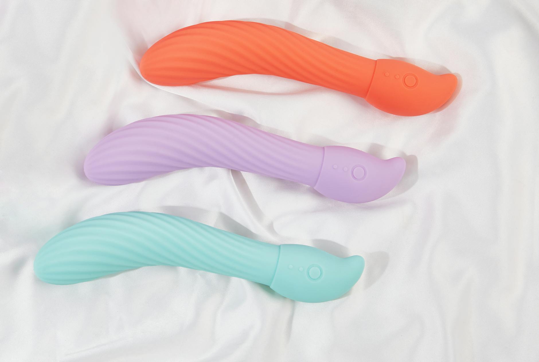 Three colorful vibrators arranged on white fabric, highlighting their smooth texture