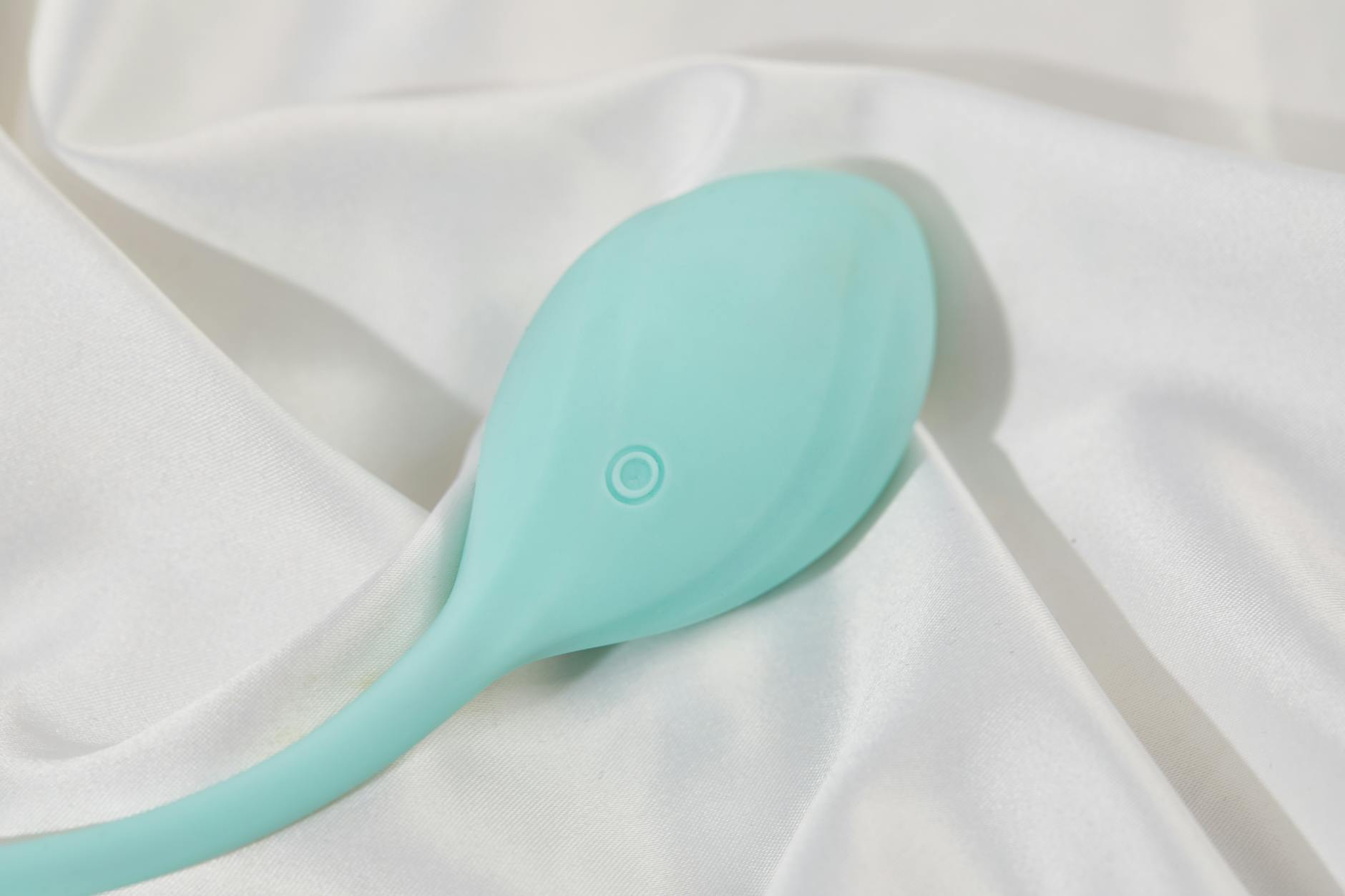 A stylish teal vibrator on smooth white silk fabric, perfect for intimate self-care.