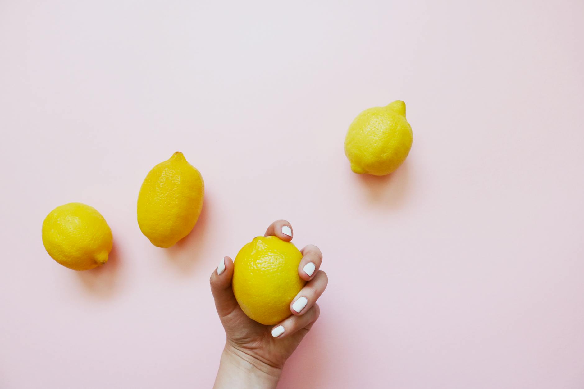 A hand holding a bright yellow lemon on soft pink background, symbolizing natural pleasure and self-acceptance
