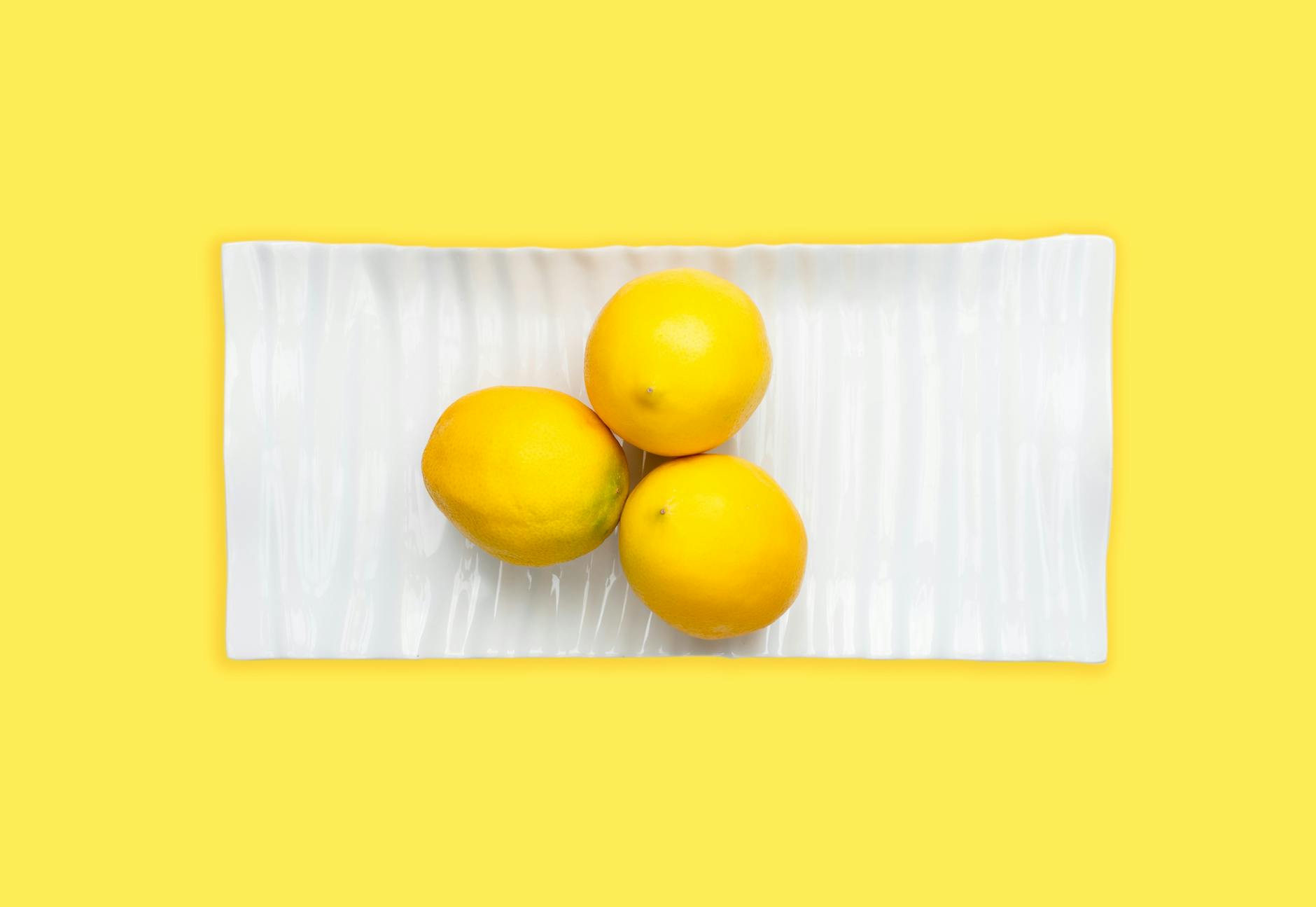 Fresh lemons arranged on a white plate with yellow background, symbolizing freshness and shared pleasure