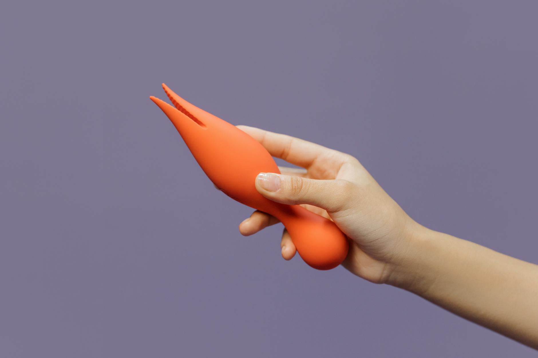 A hand holding a lemon-colored vibrator against a minimalistic purple backdrop