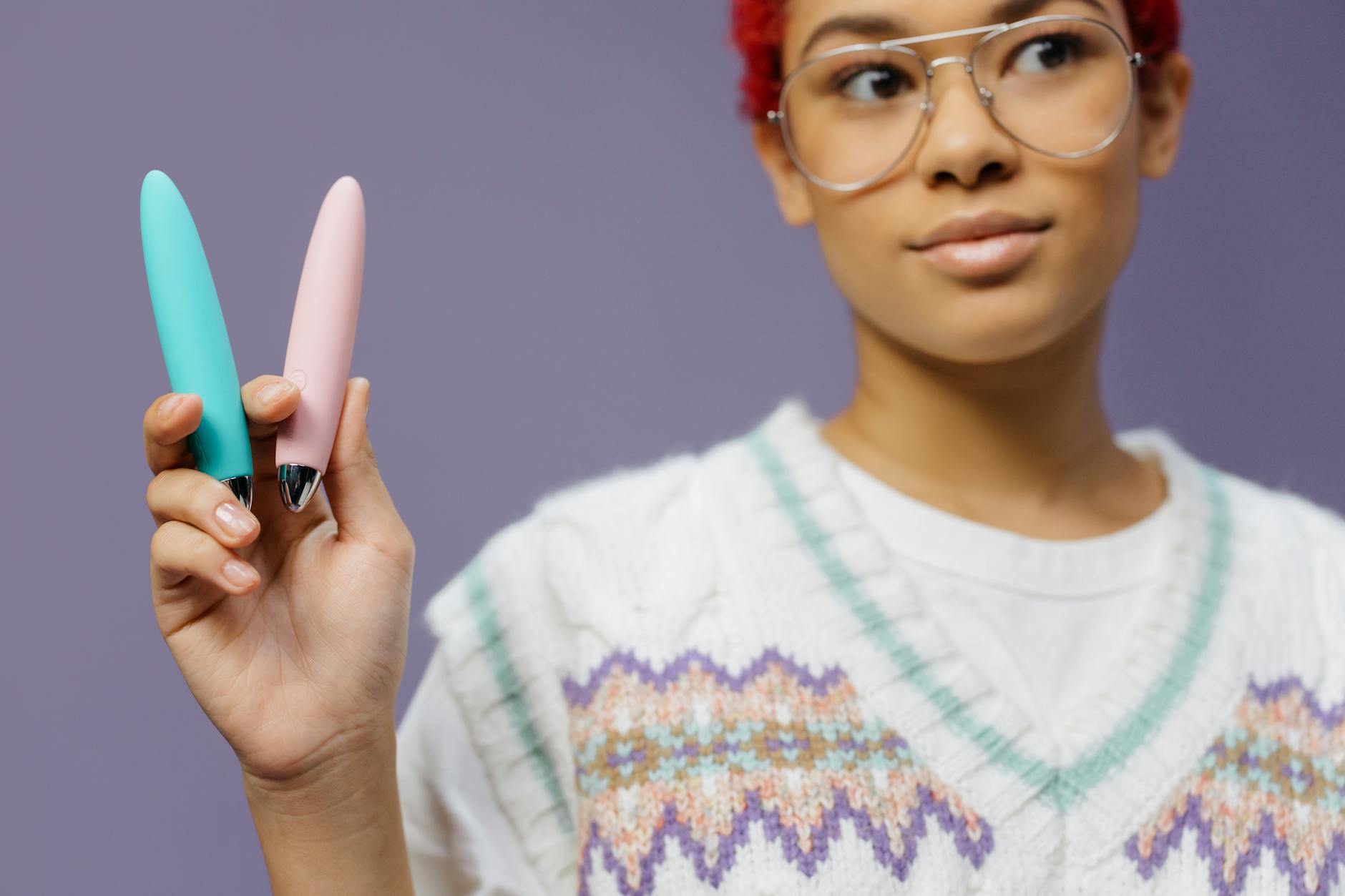 Woman holding colorful vibrators against purple background, representing courage to introduce toys