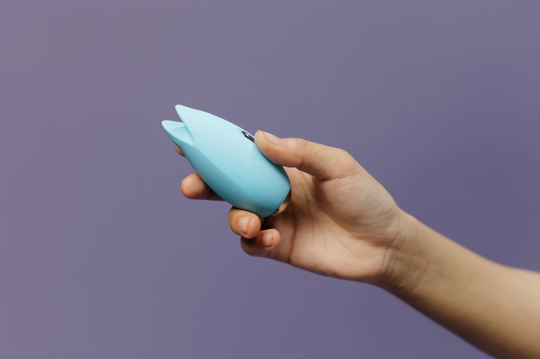 A silicone clitoral vibrator held in hand against a solid background, promoting self-love and pleasure.