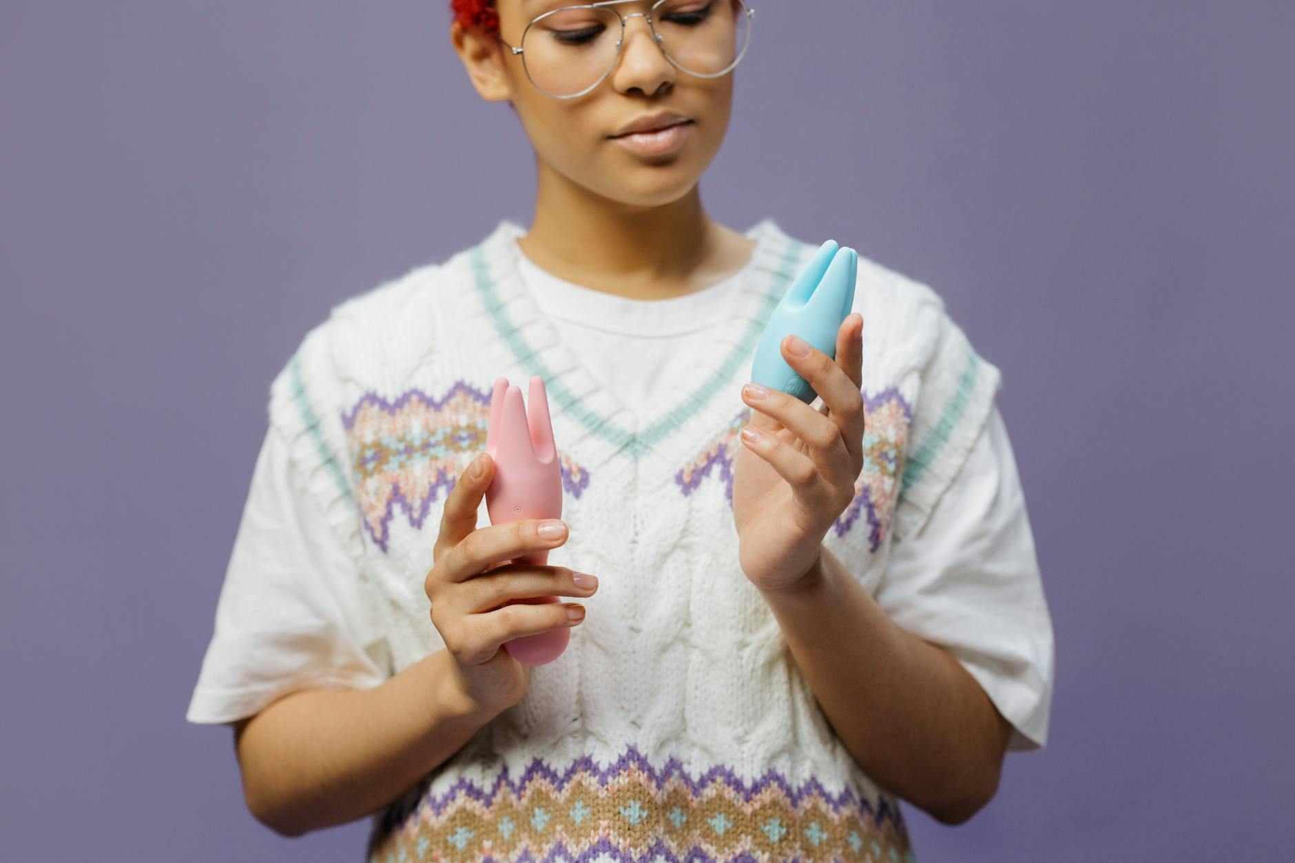 Woman holding blue and pink silicone vibrators in a contemplative manner during recovery.