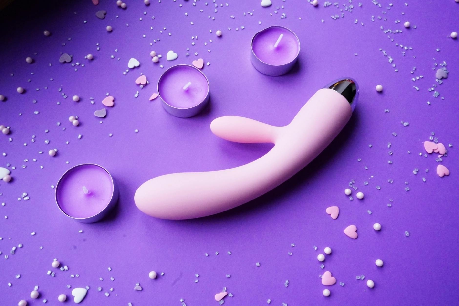 Pink vibrator on purple background with romantic candles and heart confetti